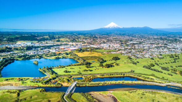 Aerial view on a New Plymouth residential suburb surrounded by green meadow with Mount Taranaki on the background. New Zealand